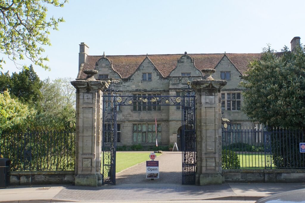 St John's House, a gabled stone Jacobean house behind iron gates and stone gateposts