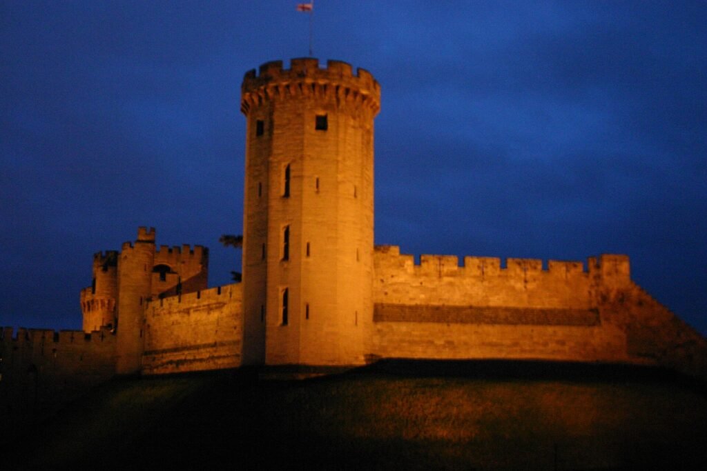Warwick Castle's walls and a tower floodlit against a dark blue night sky