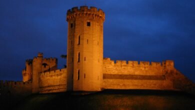Warwick Castle's walls and a tower floodlit against a dark blue night sky